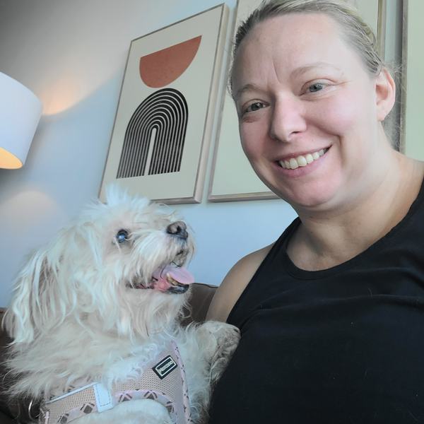 Allie smiling with a fluffy white dog in a pink harness