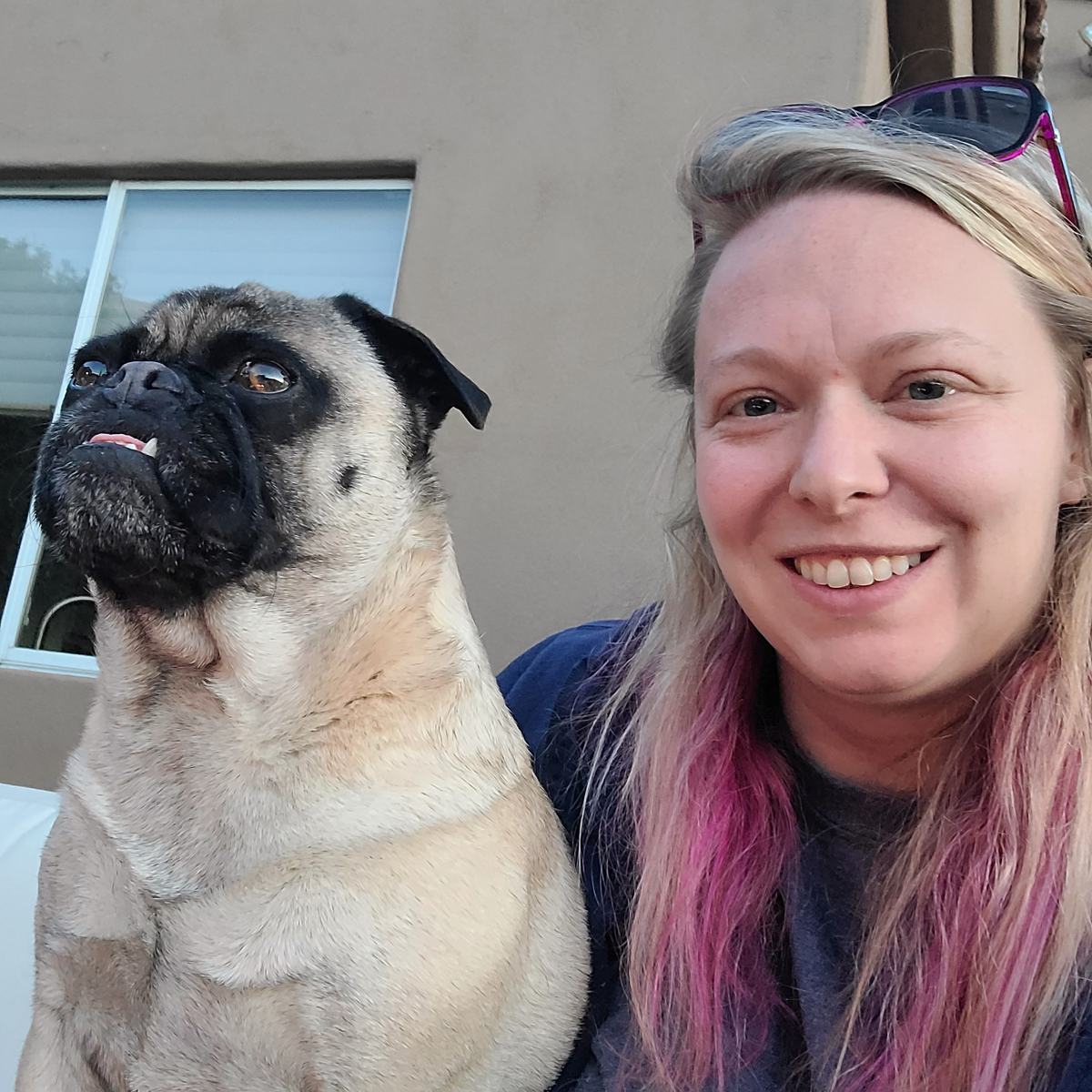 Allie smiling outdoors next to a fawn pug
